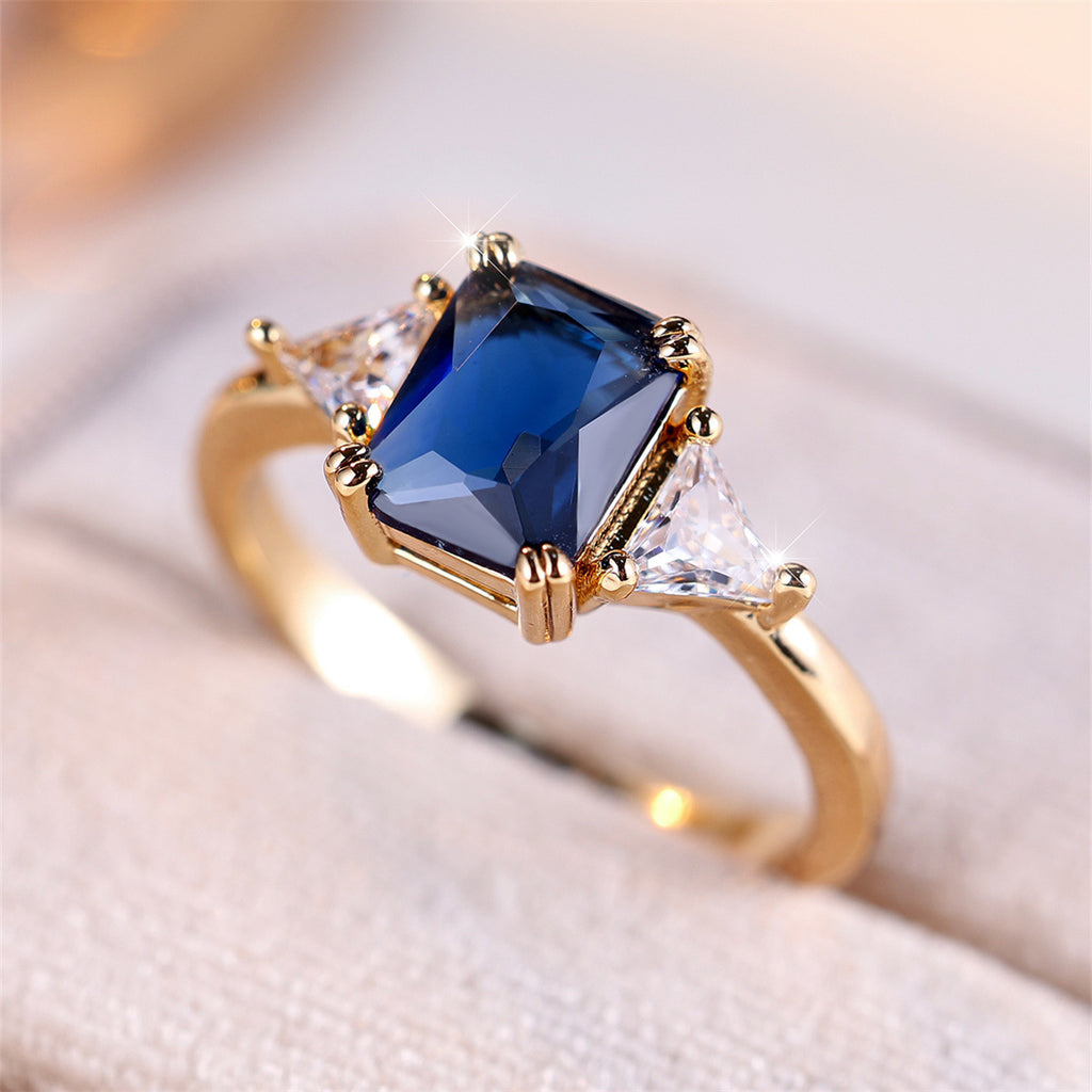 Gold ring with a blue gemstone and clear stones on a soft fabric background