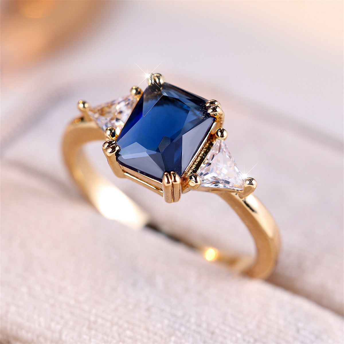 Gold ring with a blue gemstone and clear stones on a soft fabric background