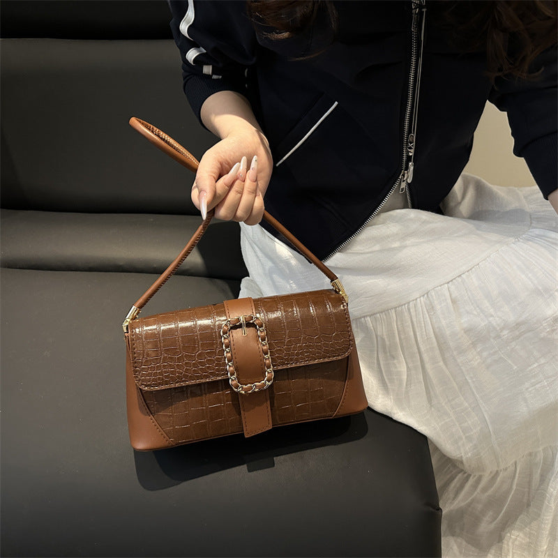 Brown handbag with chain detail held by a person on a dark surface