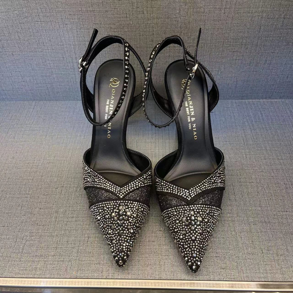Black high-heeled shoes with rhinestone details on a gray surface