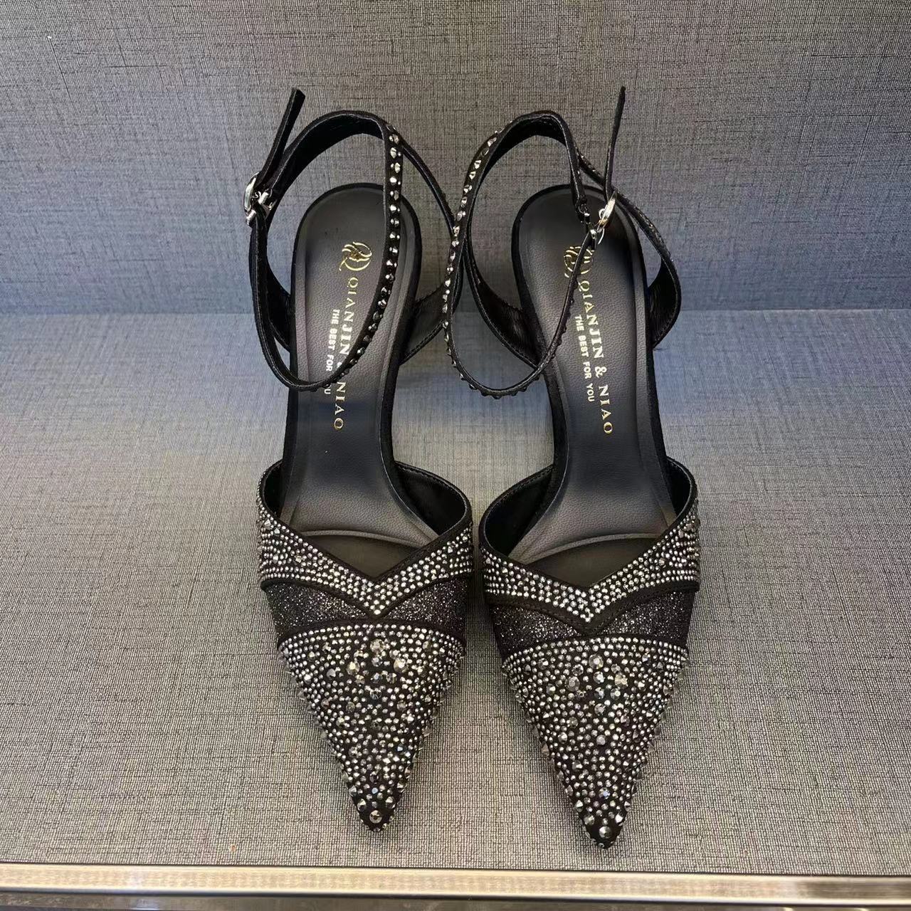 Black high-heeled shoes with rhinestone details on a gray surface