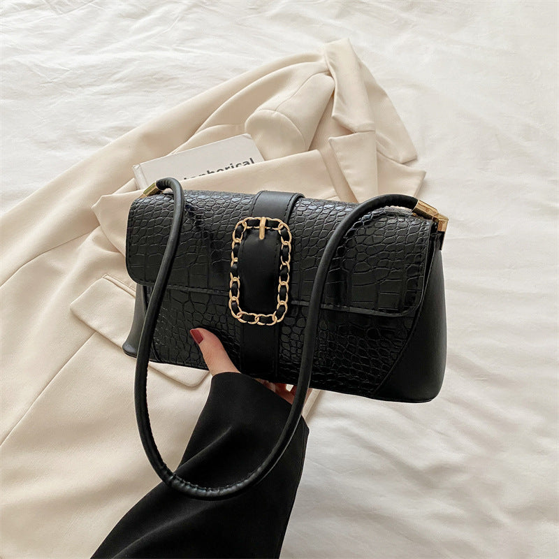 Black handbag with gold chain detail held by a hand on a light background