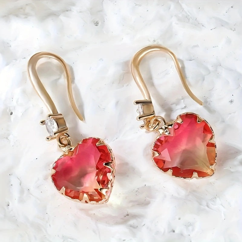 Gold earrings with red heart-shaped gemstones on a white textured background
