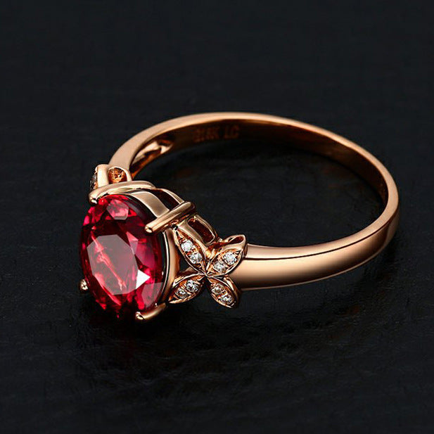 Rose gold ring with a red gemstone and butterfly design on a dark background