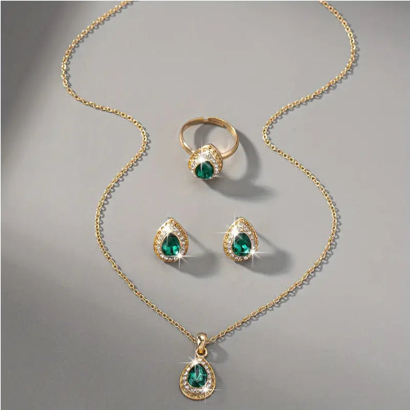 Gold jewelry set with emerald green gemstones on a gray background