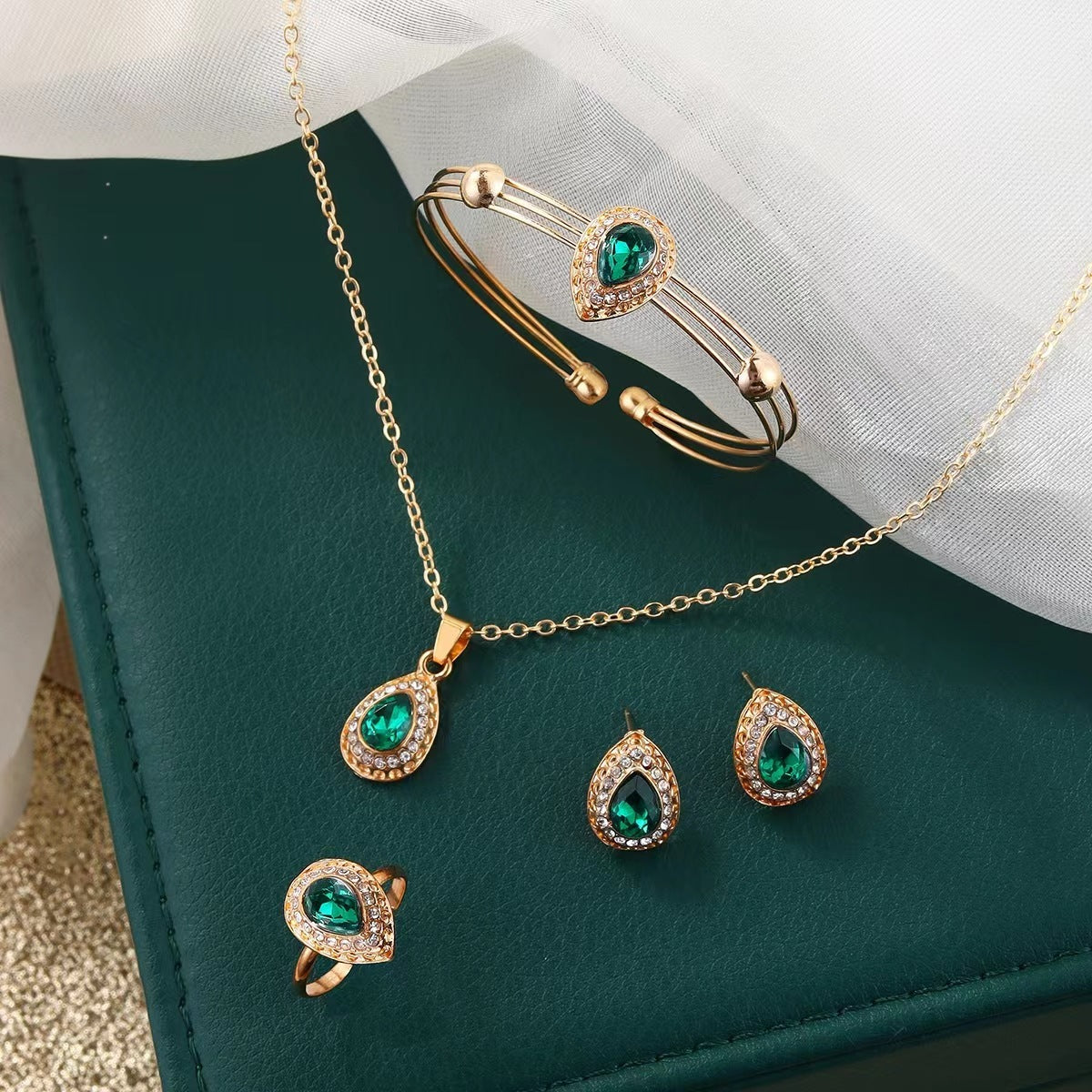 Jewelry set with necklace, earrings, and ring featuring green gemstones on a green surface.