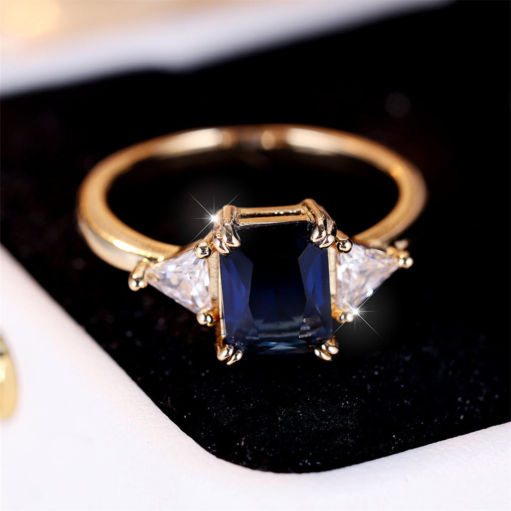 Gold ring with a blue gemstone and two triangular diamonds on a black background