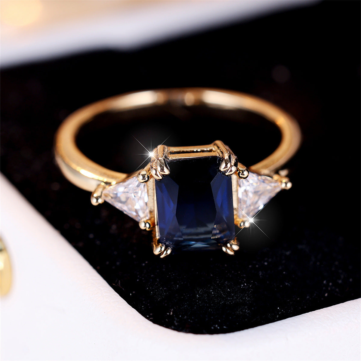 Gold ring with a blue gemstone and two triangular diamonds on a black background