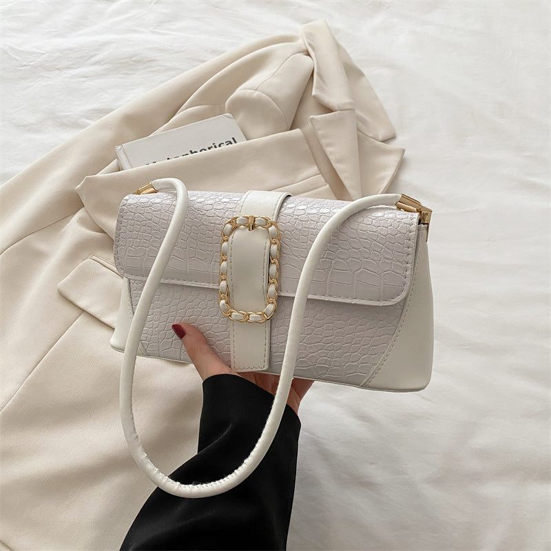 White textured handbag with gold accents held by a hand on a light background