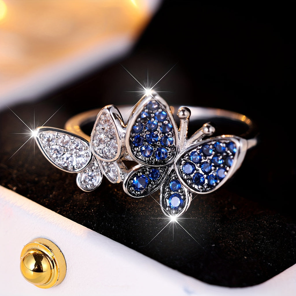 Butterfly-shaped ring with blue and clear gemstones on a reflective surface
