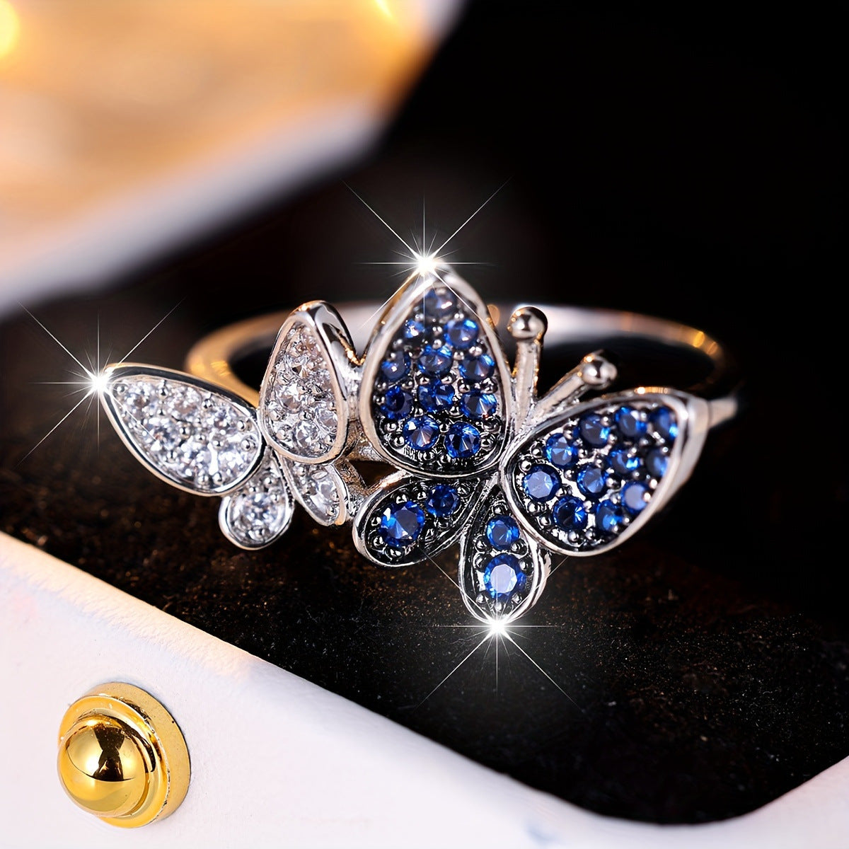 Butterfly-shaped ring with blue and clear gemstones on a reflective surface