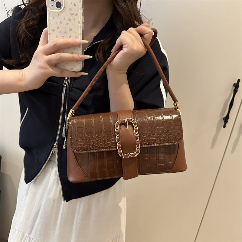 Person holding a brown handbag with a gold buckle against a neutral background