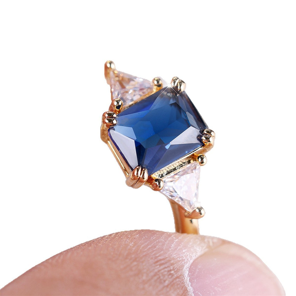 Gold ring with a blue gemstone held between fingers on a white background