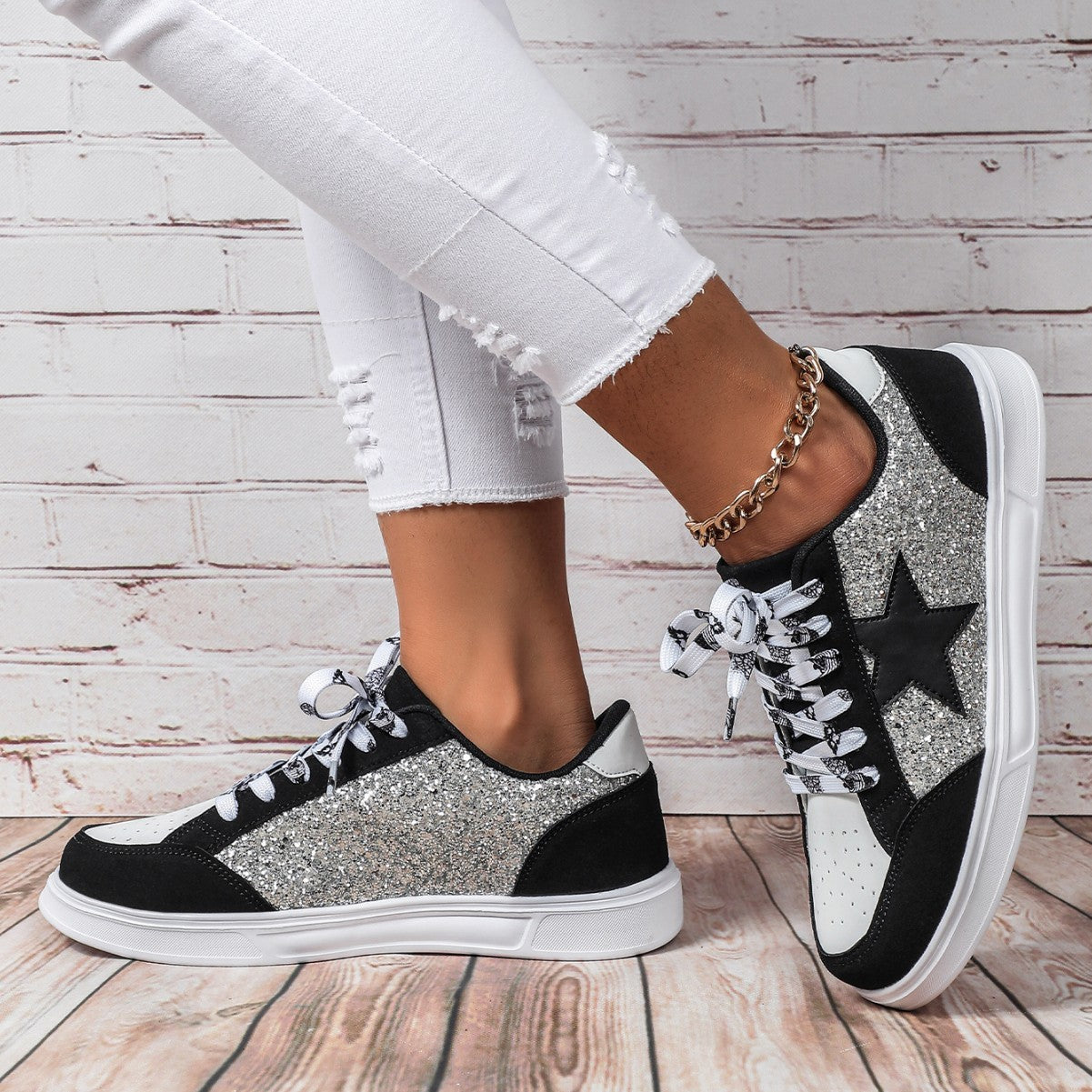 Black, white, and silver glitter sneakers worn with white jeans on a wooden floor.