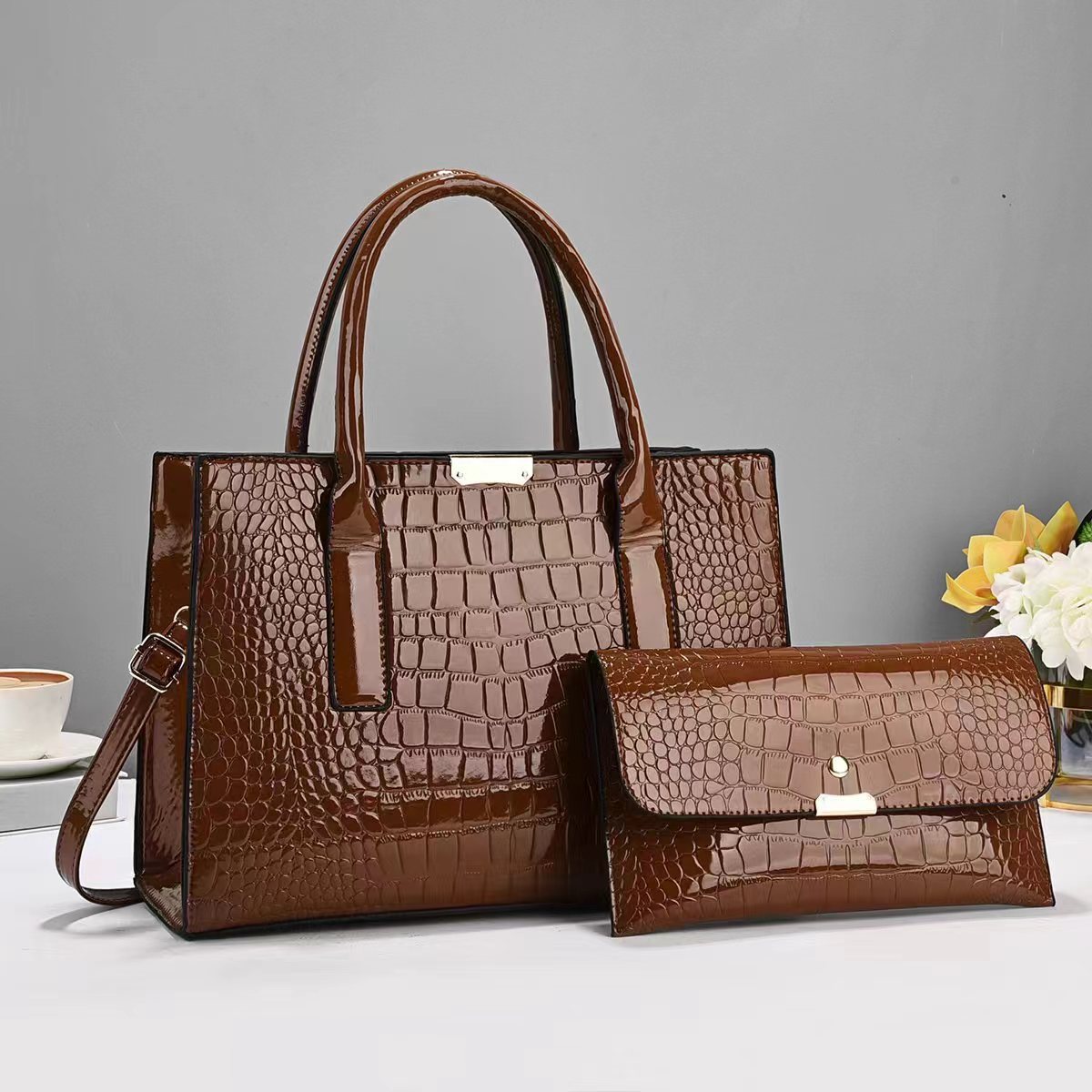 Brown crocodile-patterned handbag and wallet on a gray background