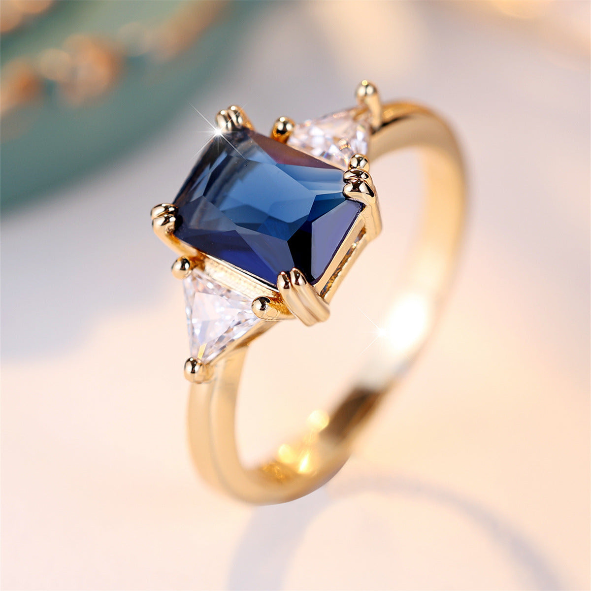 Gold ring with a blue gemstone and clear stones on a blurred background