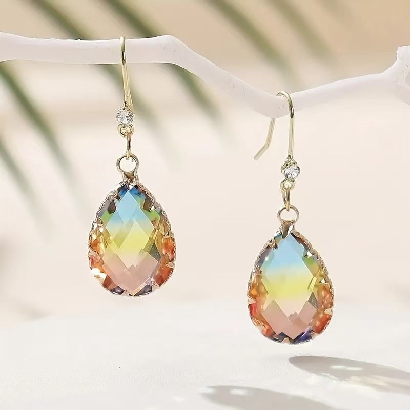 Multicolored teardrop earrings on a white branch with a blurred natural background