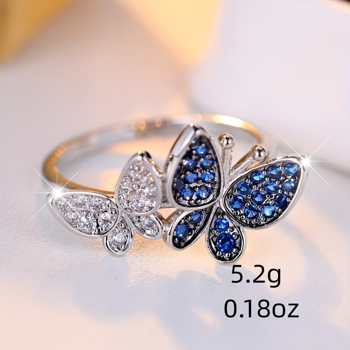 Butterfly-shaped ring with blue and clear gemstones on a light background
