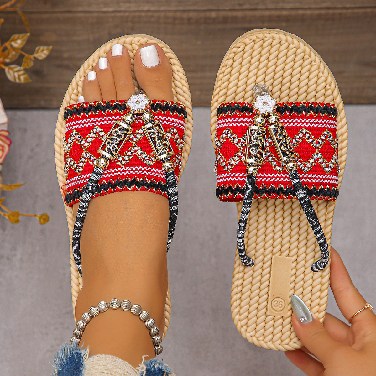 Beaded sandals with red and black pattern held by a hand against a neutral background