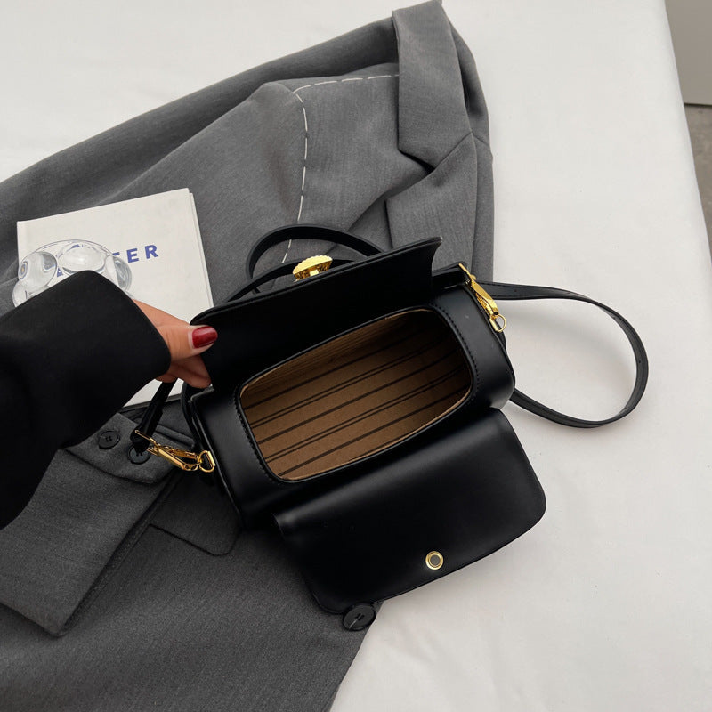 Black handbag with gold accents held by a hand on a gray suit jacket and white surface.