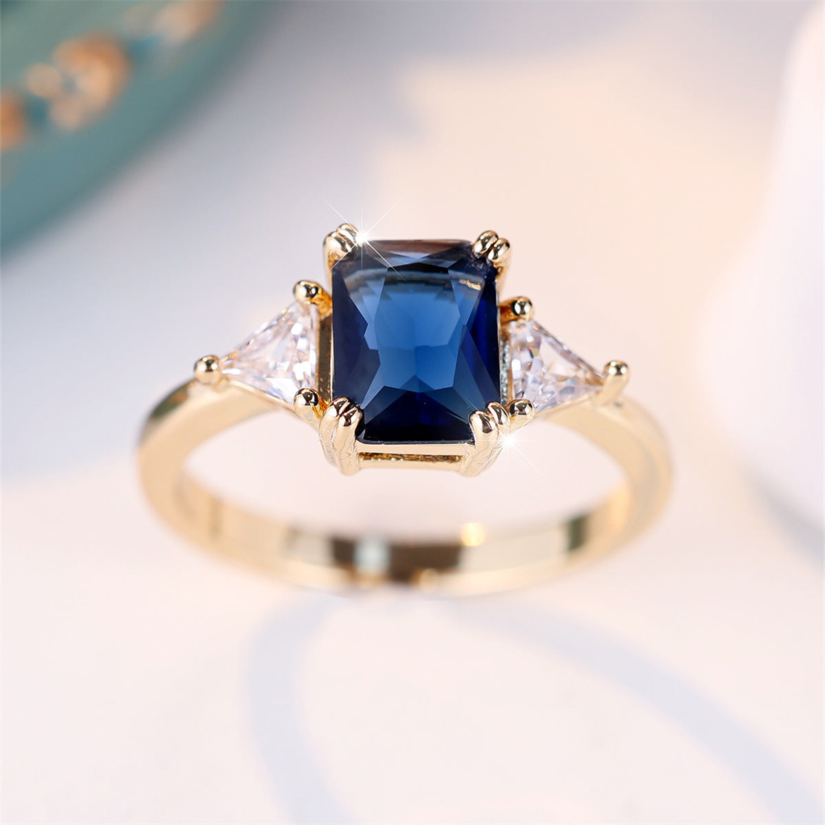 Gold ring with a blue gemstone and two smaller clear stones on a blurred background