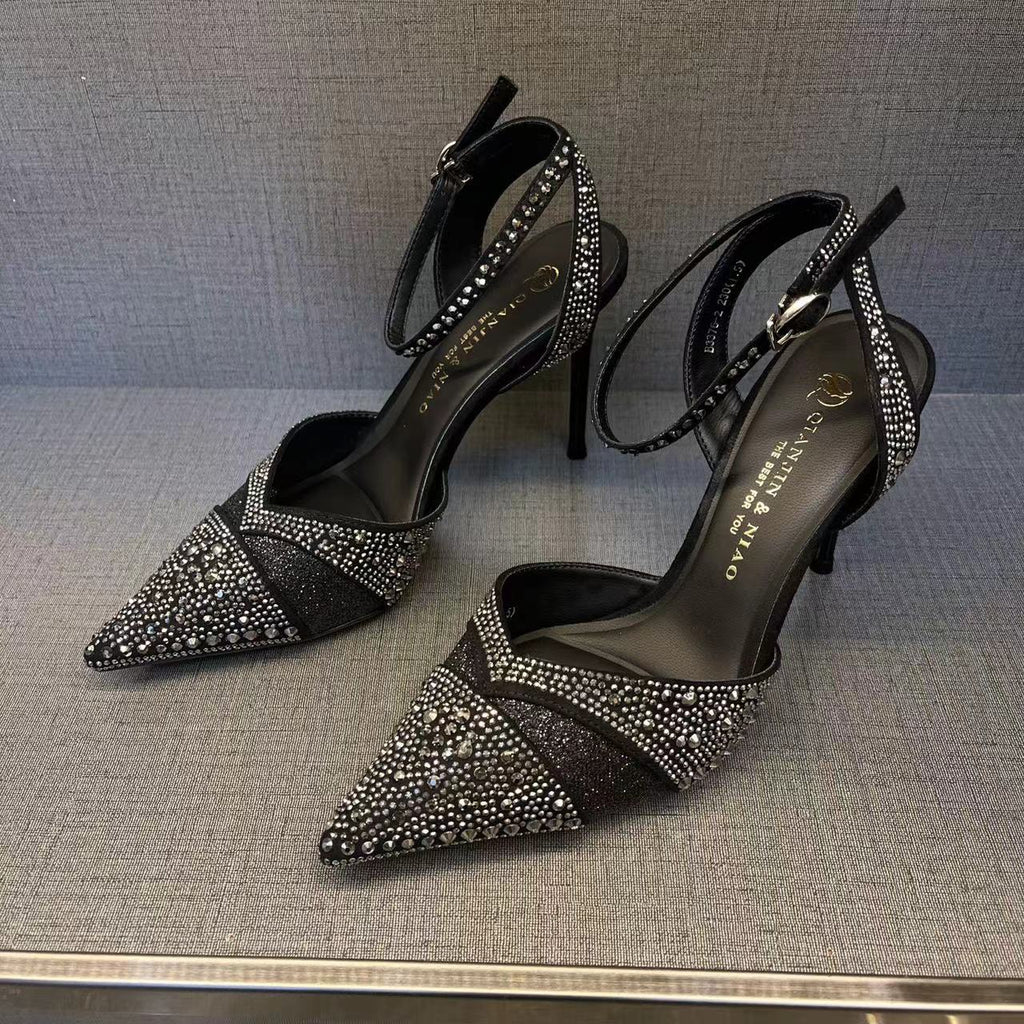 Black high-heeled shoes with rhinestone detailing on a textured surface