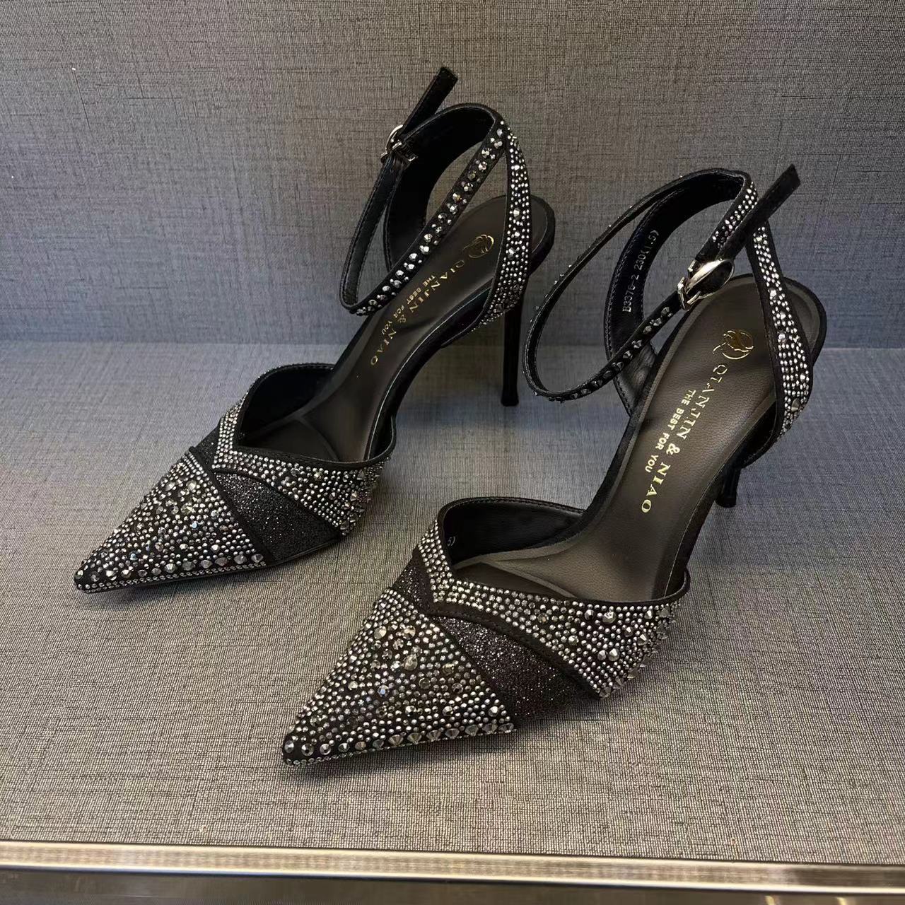 Black high-heeled shoes with rhinestone detailing on a textured surface