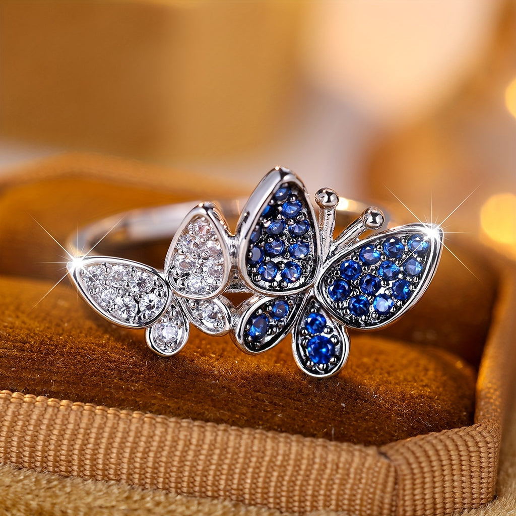 Butterfly-shaped ring with blue and clear gemstones on a wooden surface