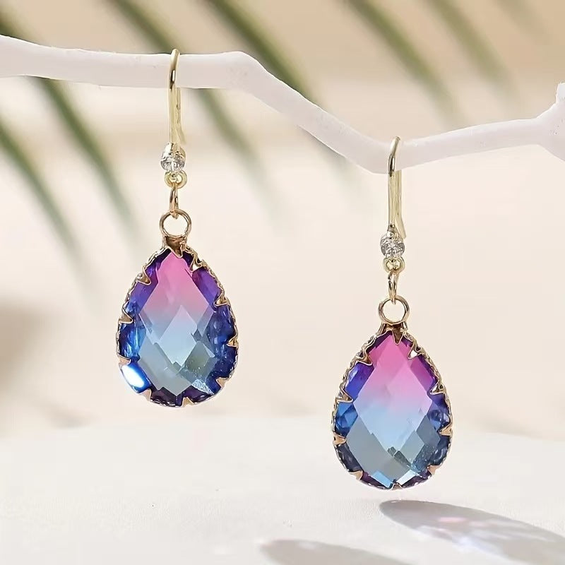 Multicolored teardrop earrings on a white stand with a blurred natural background