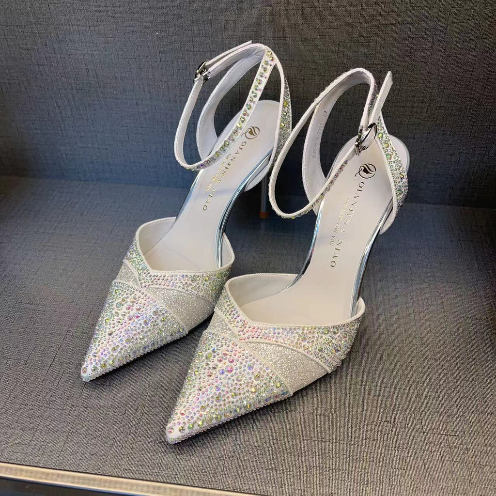 Pair of silver high-heeled shoes with rhinestone embellishments on a gray surface.